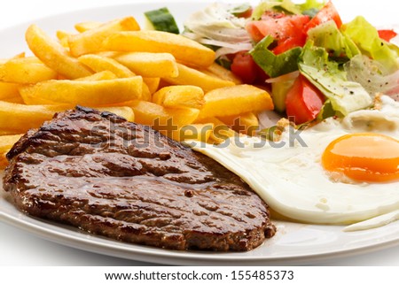 Grilled steaks, French fries, fried egg and vegetables