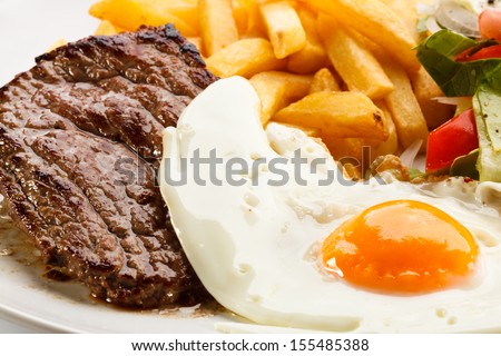 Grilled Steaks, French Fries, Fried Egg And Vegetables