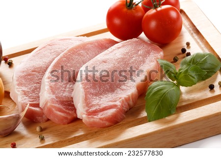 Raw pork chops on cutting board and vegetables on white background
