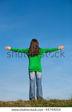 Girl standing with open arms against the blue sky