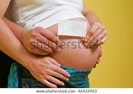 Belly of a pregnant woman with father and mother hands holding greeting card