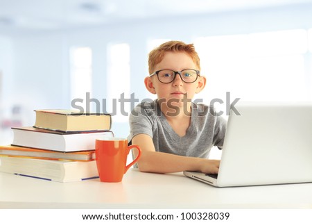 Portrait of a cute boy sitting in the school and learning on his laptop computer