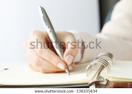 Close-up of female hand holding a pen and writing some research notes in the appointment book