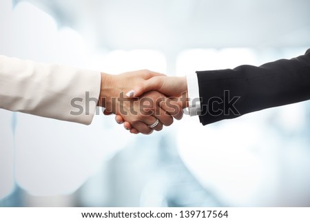 Deal! Close-up of two businesswomen shaking hands against an office backgrounds. Focus on hands