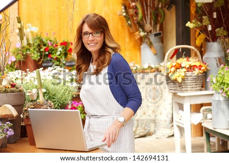 Smiling Mature Woman Florist Small Business Flower Shop Owner.  She is using laptop to take orders for her store. Shallow Focus.