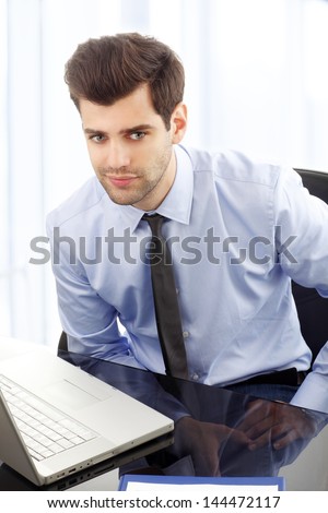 Young smiling businessman sitting in office with laptop on desk