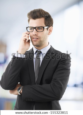 Portrait of a businessman in office, using his mobile phone with arms crossed