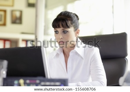 A woman in her mid thirties sits at a desk in front of a laptop screen.