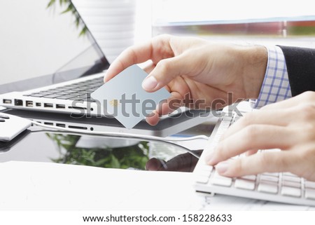 Young business man typing in credit card info on a computer keyboard. Credit card visible in hand.