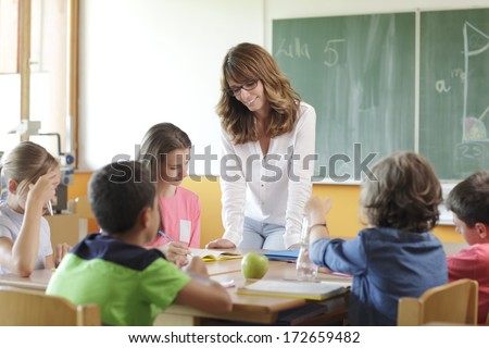 Elementary Classroom Setting. Focus On Teacher And Chalkboard.
