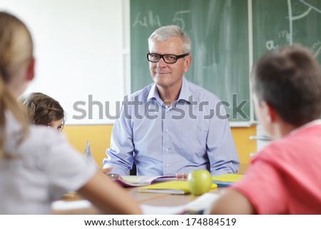 Elementary classroom. Focus on teacher sitting in front of chalkboard.