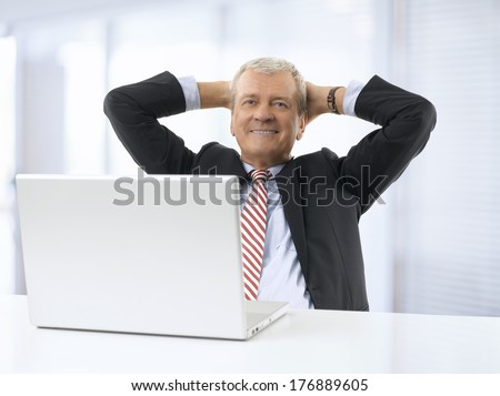 Portrait of relaxed senior businessman sitting in office. He wears shirt and tie.