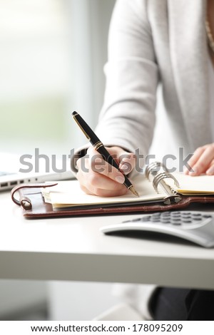 Close-up of businesswoman holding pen in hands and writing a note.