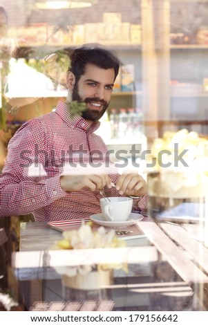 Close-up portrait of young man sitting at table in coffee shop. Shot behind the window.