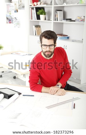 Young businessman sitting at desk and working in small architect studio.