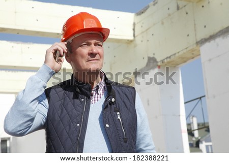 Close-up of construction worker standing and using his mobile in front of construction site.