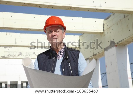 Senior architect standing in front of building, while using his mobile. Small business.