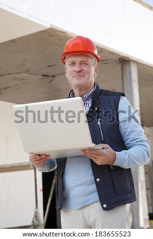 Senior architect standing in front of building, while using his mobile. Small business.