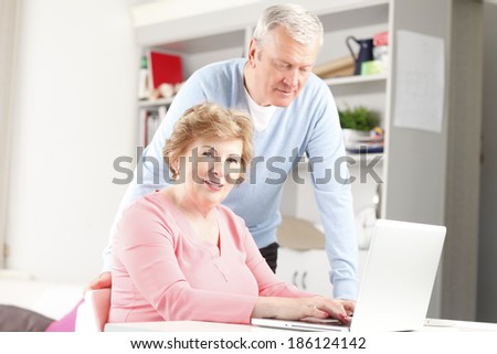 Happy senior couple sitting at desk and planning for retirement at home. They surfing on internet with laptop