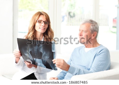 Beautiful female doctor analyzing x-ray with senior patient at small clinic.