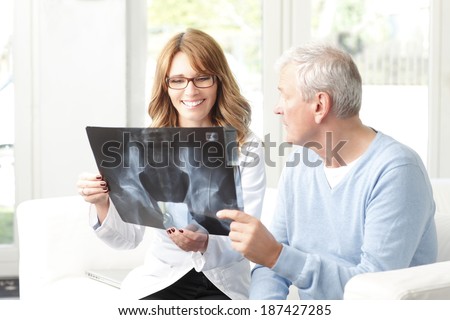 Happy female doctor analyzing x-ray with senior patient at small clinic.