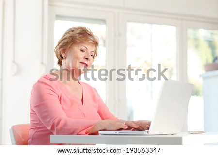 Portrait of senior woman sitting at desk and working on laptop.