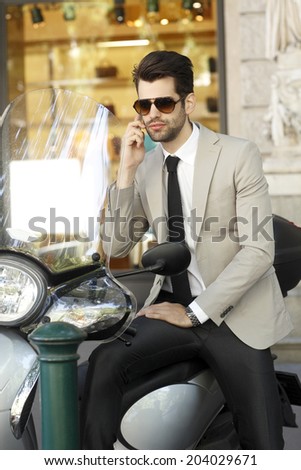 Portrait of young modern businessman using his mobile, while sitting on scooter.