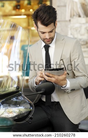 Portrait of modern businessman with digital tablet, sitting on scooter at the city. Business people.