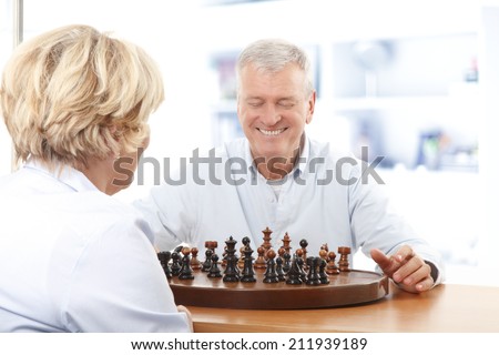 Happy senior couple sitting at desk and playing chess at home. Leisure activity at nursing home.