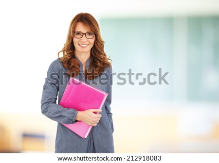Happy teacher with notebook standing in front of black board at classroom.