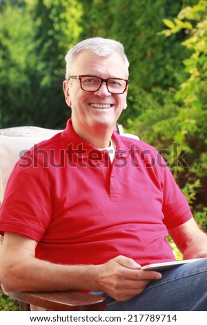 Portrait of senior businessman sitting at home in garden and working on digital tablet.