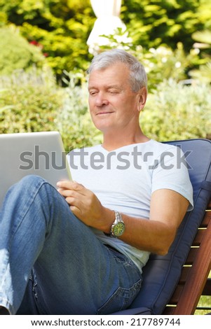 Portrait of active senior businessman sitting at garden and working at home with digital tablet.