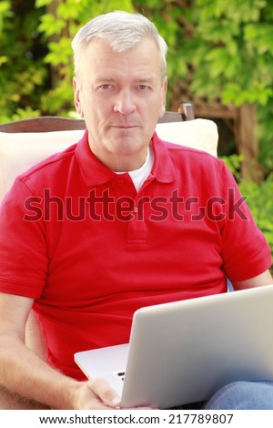 Old people sitting at nursing home garden, while using his laptop.