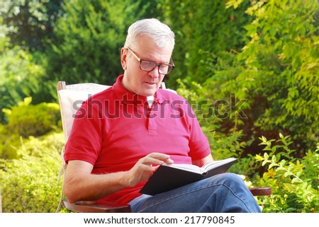 Portrait of old man reading book in garden at home.