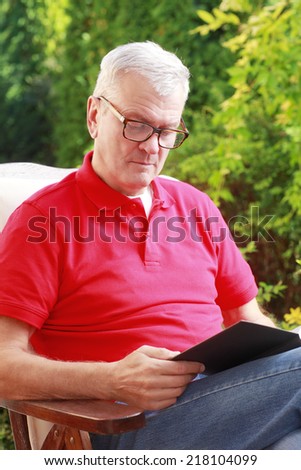 Casual old man reading book in garden.