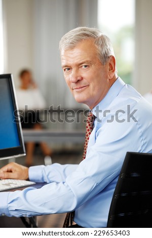 Close-up portrait of old businessman sitting at office while using computer. Business people.
