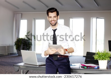 Portrait of casual young broker sitting at desk while using digital tablet. Business people.