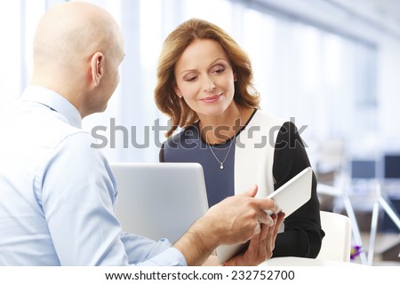 Executive broker holding tablet while presenting plan to middle age business woman. Business meeting.