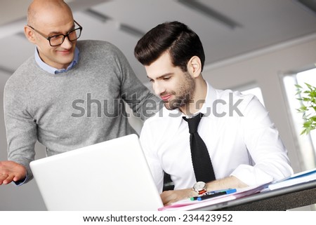 Senior businessman giving advise to his colleagues while writing annual report on laptop.