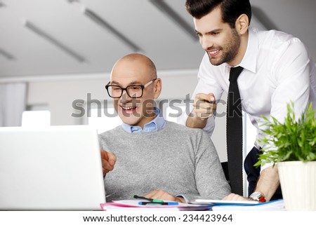 Senior businessman giving advise to his colleagues while writing annual report on laptop.