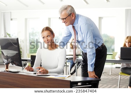 Old businessman helping solution problem to business woman while sitting at office in front of laptop. Teamwork.