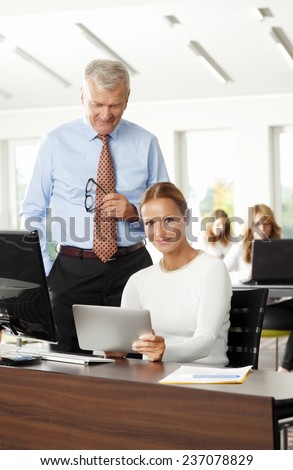 Beautiful business woman holding digital tablet in her hands while working on project with old businessman.