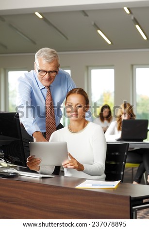 Business woman holding laptop and working with old businessman while sitting at meeting.