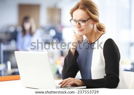 Mature business woman thinking in front of laptop while sitting at office.