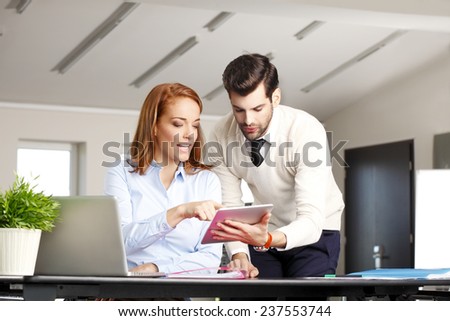Portrait of mature business woman holding digital tablet and giving advice to young businessman at office. Teamwork.