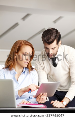 Portrait of mature business woman holding digital tablet and giving advice to young businessman at office. Teamwork.