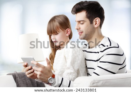 Young father teaching his daughter how to use digital tablet safety while they are sitting at home at sofa.