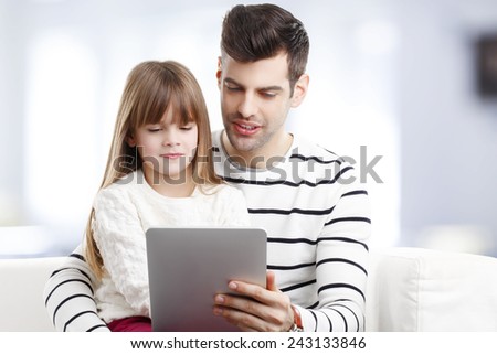 Young father teaching his daughter how to use digital tablet safety while they are sitting at home at sofa.