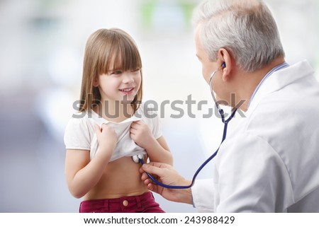 Senior male doctor listening heart break of preschool child at private clinic.