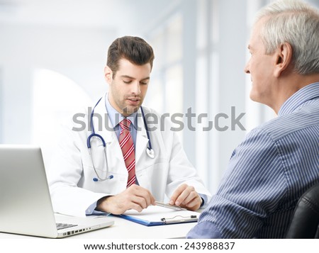 Young male doctor consulting with old patient at nursing home.